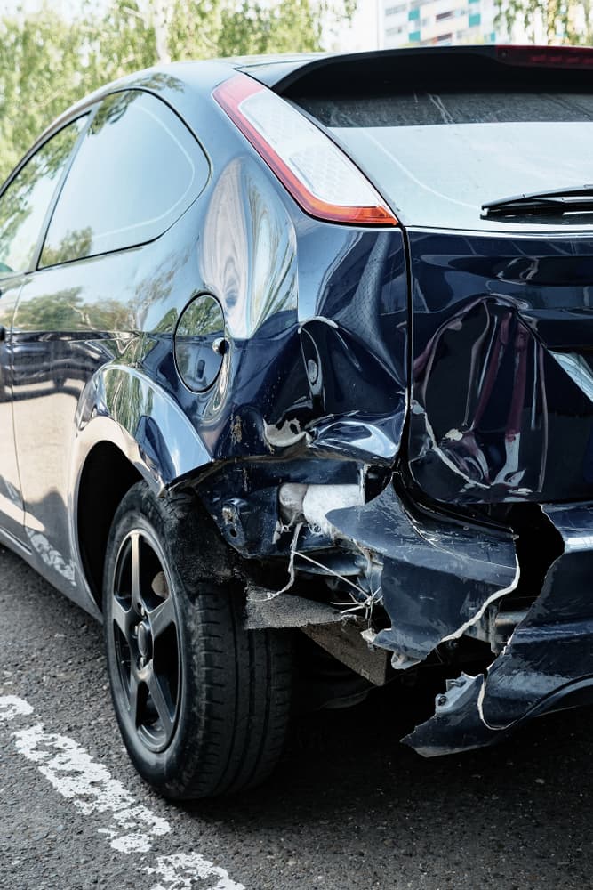Dented rear hood of a blue car, showcasing vehicular damage.