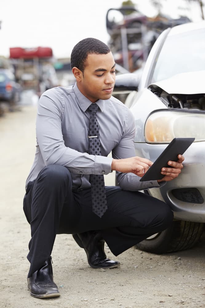 Insurance adjuster digitally assessing car wreck with tablet during inspection for insurance claim after an accident.