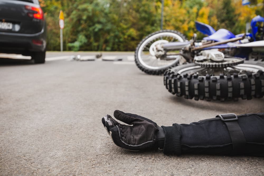 A motorcycle accident scene showing a fallen rider’s arm and a dirt bike lying on the road, illustrating the aftermath of a serious crash in