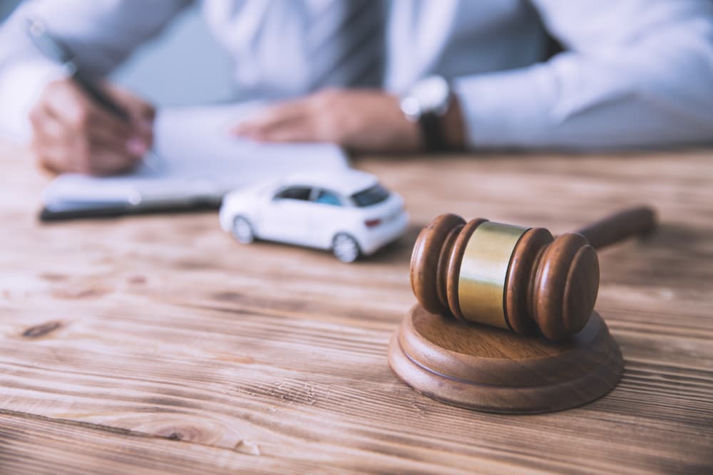 Legal professional writing on document near gavel and toy car.