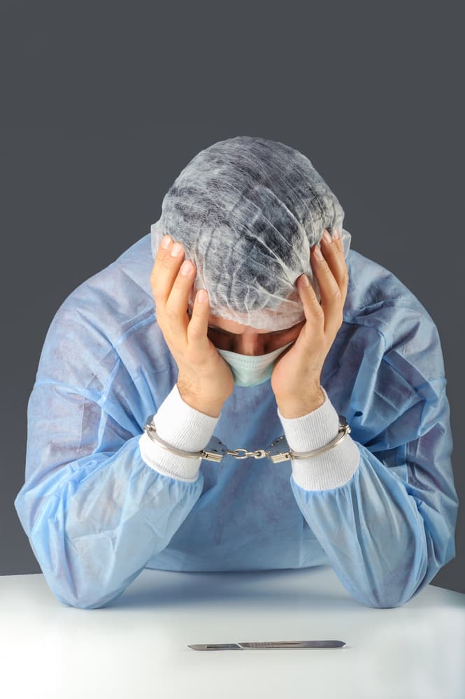 A medical professional with handcuffs is distressed, with a scalpel on the table.