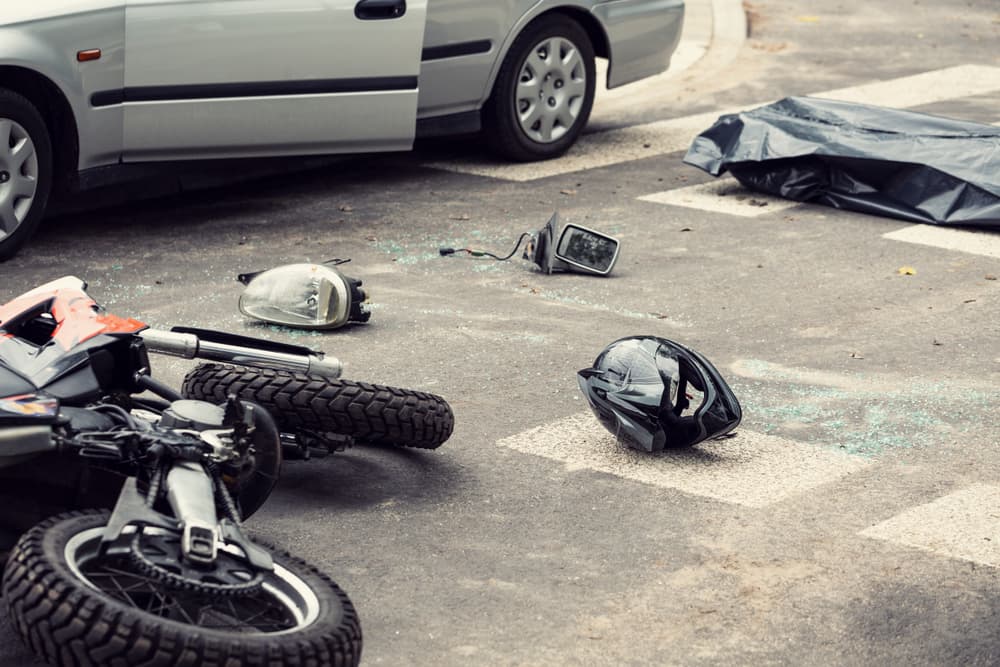Black helmet and motorcycle lie on the road after a deadly crash involving a car.